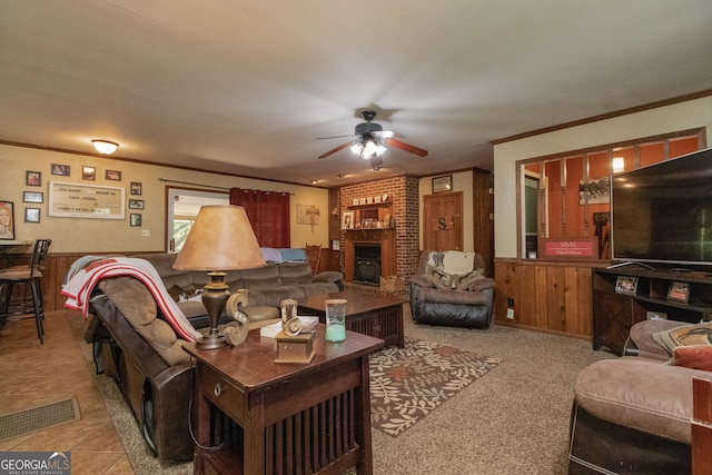 living room with wood walls, crown molding, a brick fireplace, ceiling fan, and light colored carpet