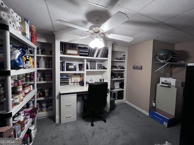 office featuring carpet floors, ceiling fan, built in desk, and a drop ceiling