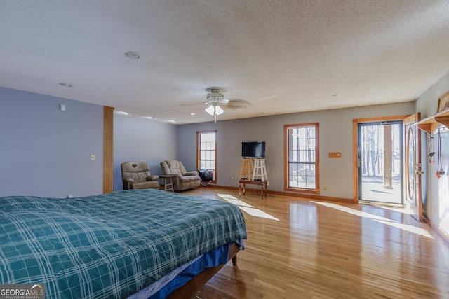 bedroom with ceiling fan, access to exterior, a textured ceiling, and light hardwood / wood-style flooring