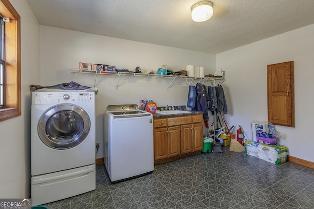 clothes washing area featuring washing machine and clothes dryer, sink, cabinets, and a textured ceiling