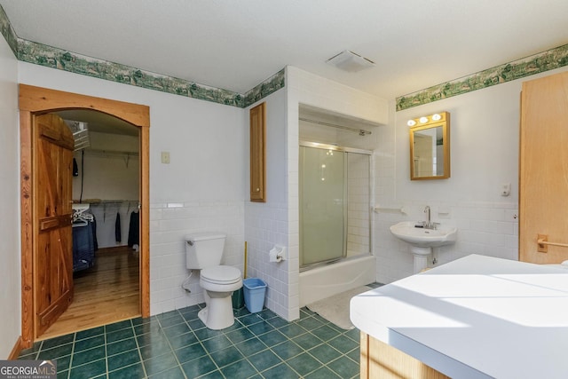 full bathroom featuring tile patterned floors, sink, shower / bath combination with glass door, tile walls, and toilet