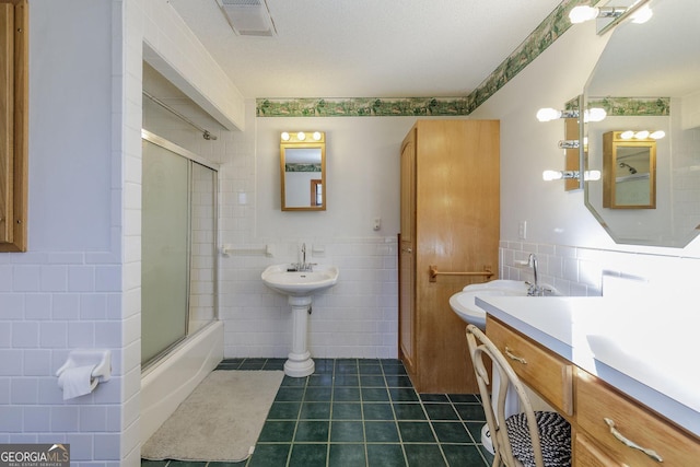 bathroom featuring bath / shower combo with glass door, sink, tile patterned flooring, a textured ceiling, and tile walls