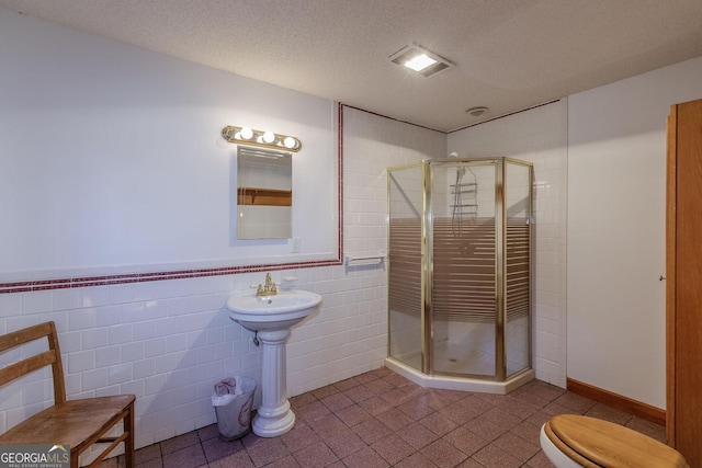 bathroom featuring a textured ceiling, toilet, tile walls, and a shower with shower door