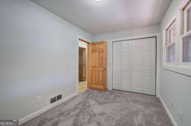 unfurnished bedroom with light carpet, a closet, and a textured ceiling