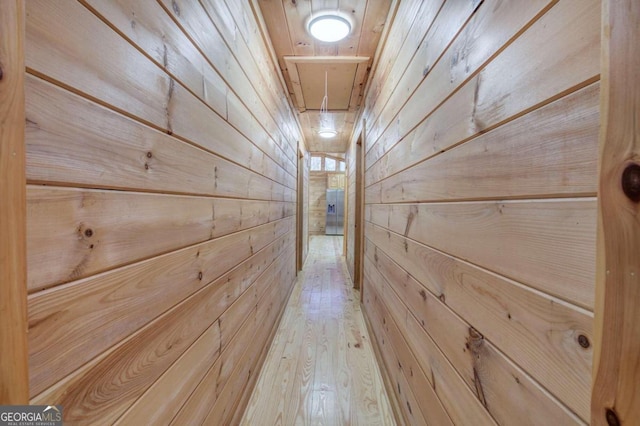 hall with light wood-type flooring and wood walls