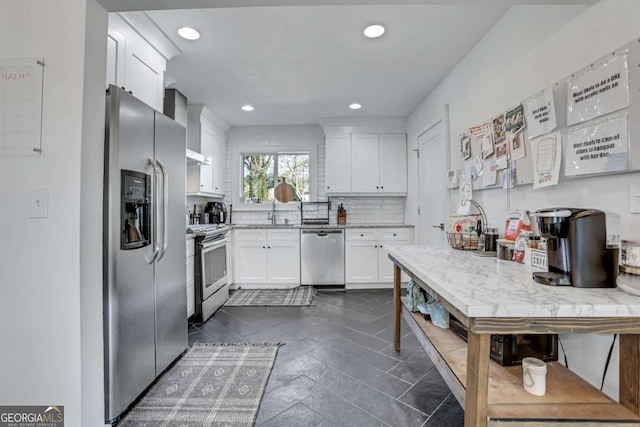 kitchen featuring appliances with stainless steel finishes, wall chimney exhaust hood, white cabinetry, and dark tile flooring