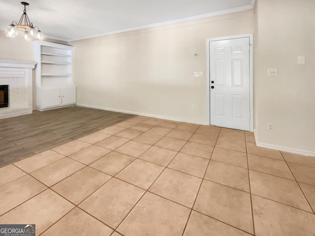 unfurnished living room featuring built in shelves, a notable chandelier, crown molding, a fireplace, and light hardwood / wood-style flooring