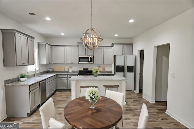 kitchen with hardwood / wood-style floors, pendant lighting, a kitchen island, gray cabinetry, and appliances with stainless steel finishes