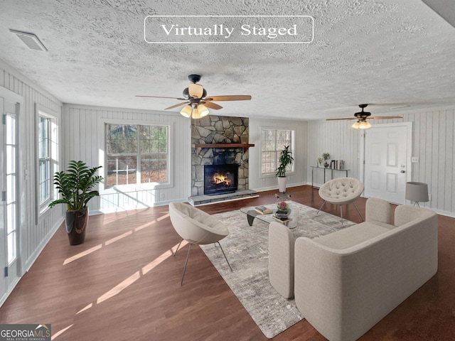 living room with hardwood / wood-style floors, a textured ceiling, ceiling fan, and a stone fireplace