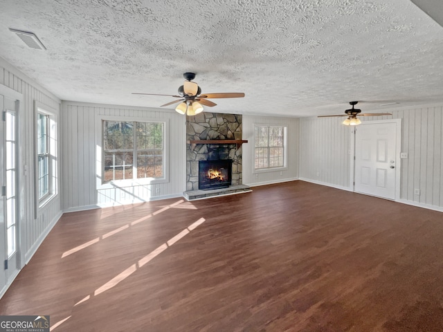 unfurnished living room with a textured ceiling, a stone fireplace, ceiling fan, and dark hardwood / wood-style floors