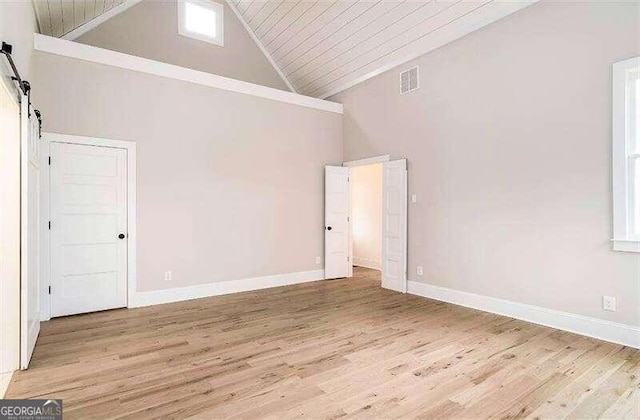 empty room featuring a barn door, high vaulted ceiling, and light hardwood / wood-style flooring