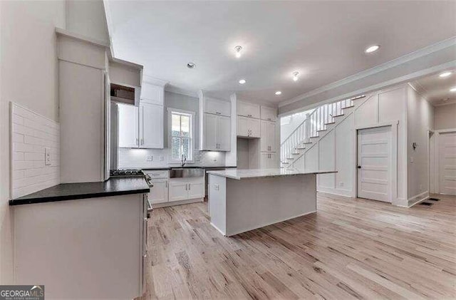 kitchen with light wood-type flooring, tasteful backsplash, a center island, sink, and white cabinets