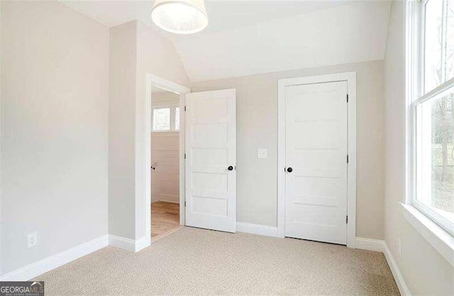 unfurnished bedroom featuring light carpet and lofted ceiling