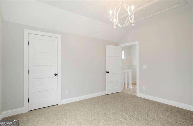 unfurnished bedroom with an inviting chandelier, light carpet, and vaulted ceiling