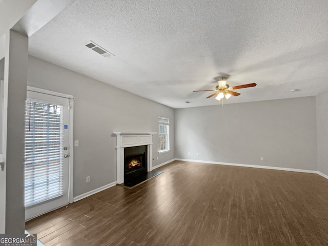 unfurnished living room featuring a textured ceiling, a healthy amount of sunlight, ceiling fan, and dark hardwood / wood-style flooring