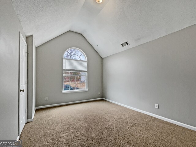 carpeted spare room with a textured ceiling and lofted ceiling