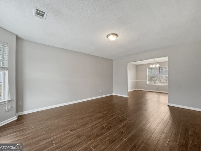 empty room with a notable chandelier, a textured ceiling, and dark wood-type flooring