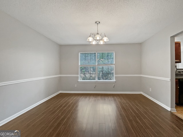 unfurnished room with a notable chandelier, a textured ceiling, and dark hardwood / wood-style floors