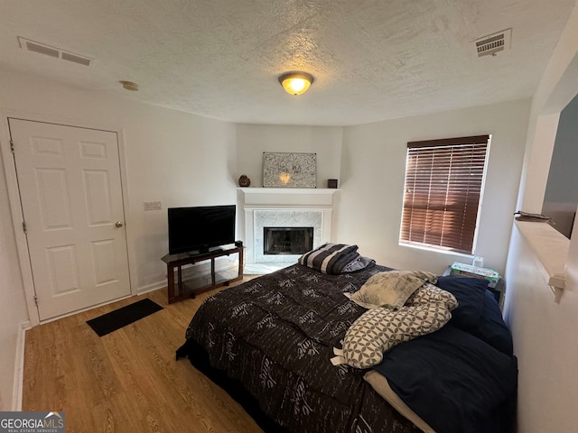 bedroom with light hardwood / wood-style flooring, a textured ceiling, and a fireplace