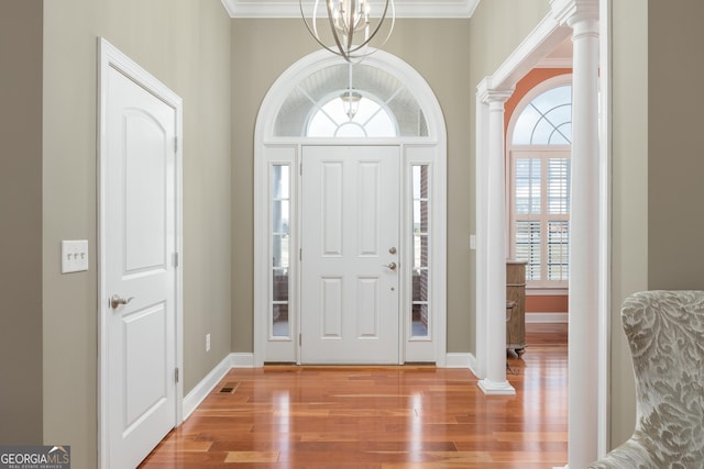 entrance foyer featuring a notable chandelier, crown molding, light hardwood / wood-style floors, and decorative columns