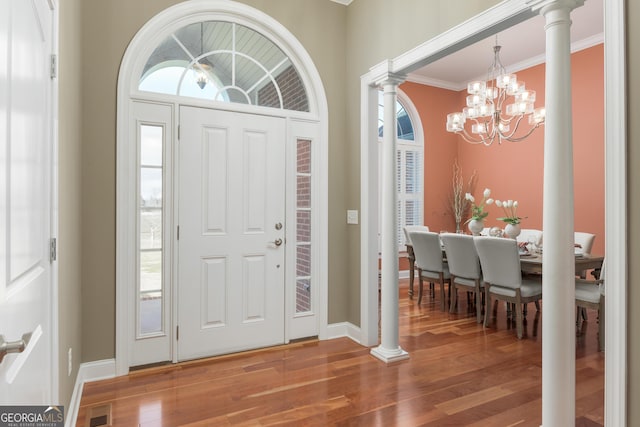 foyer with a notable chandelier, ornamental molding, decorative columns, and hardwood / wood-style flooring