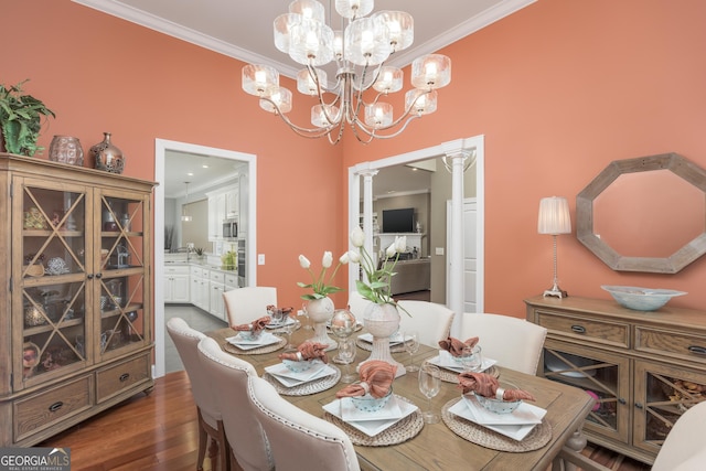 dining area with dark wood-type flooring, ornamental molding, a notable chandelier, and ornate columns