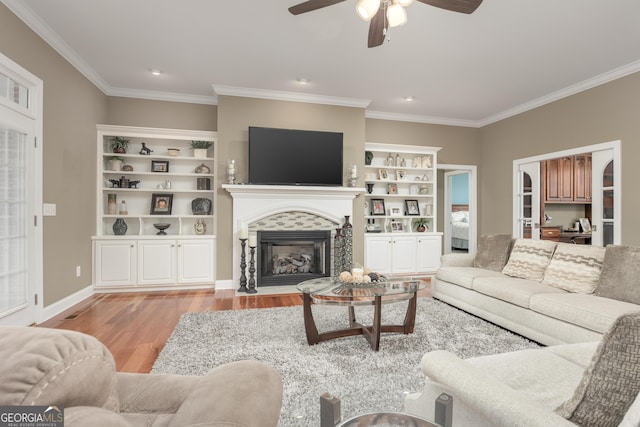 living room with built in shelves, ceiling fan, light wood-type flooring, and crown molding