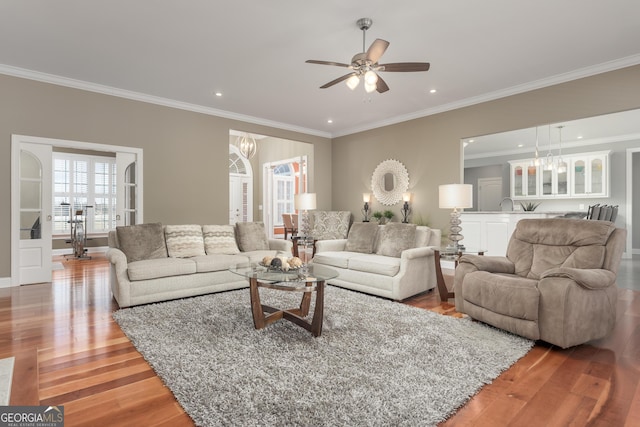 living room featuring crown molding, ceiling fan with notable chandelier, and wood-type flooring