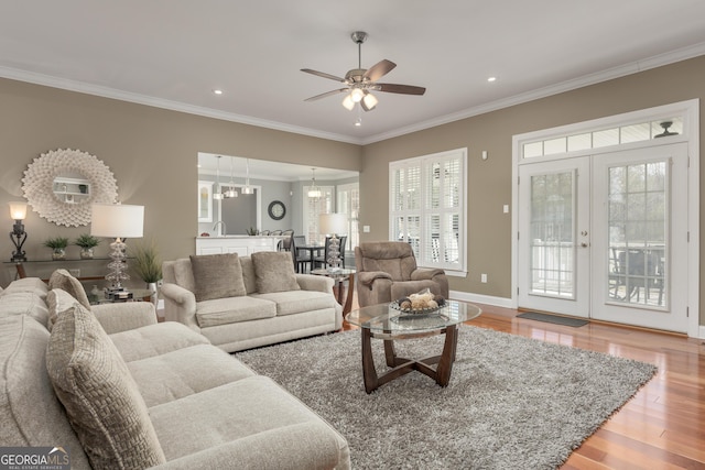 living room featuring ornamental molding, light hardwood / wood-style floors, ceiling fan with notable chandelier, and a wealth of natural light