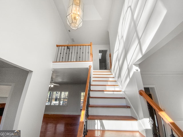 stairs with a towering ceiling, ceiling fan, and dark wood-type flooring