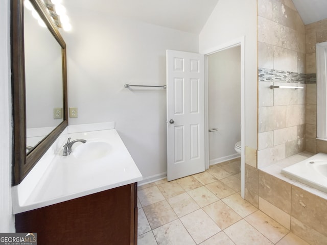 bathroom with tile flooring, vaulted ceiling, a relaxing tiled bath, toilet, and vanity