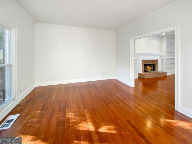 unfurnished living room featuring a brick fireplace, dark wood-type flooring, ornamental molding, and built in shelves