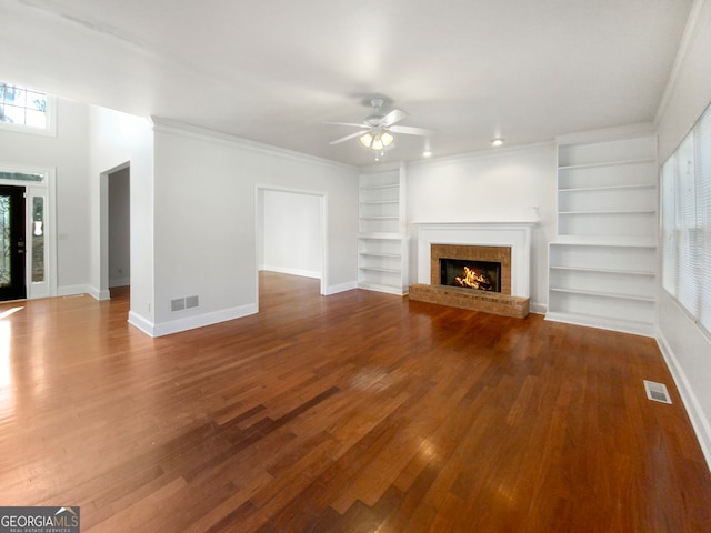 unfurnished living room with a brick fireplace, dark hardwood / wood-style floors, ceiling fan, ornamental molding, and built in shelves