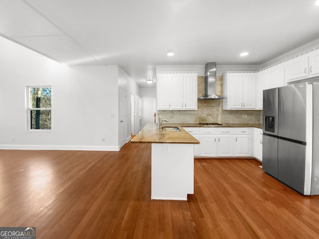 kitchen featuring stainless steel appliances, sink, hardwood / wood-style flooring, white cabinetry, and wall chimney range hood