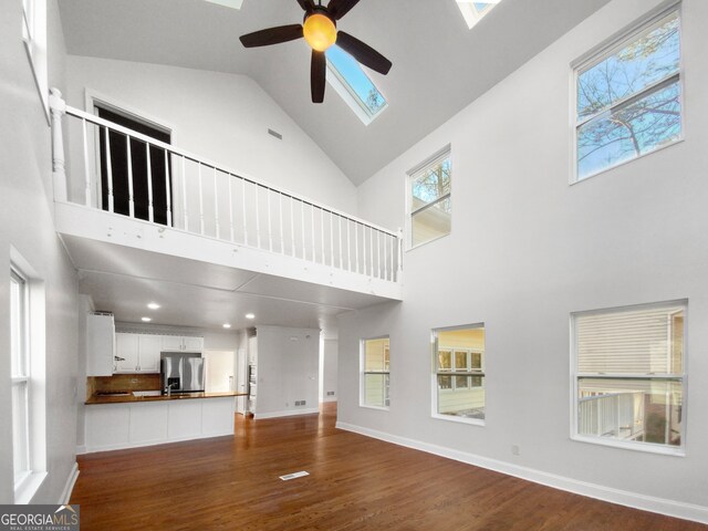 unfurnished living room featuring high vaulted ceiling, dark wood-type flooring, ceiling fan, and a skylight