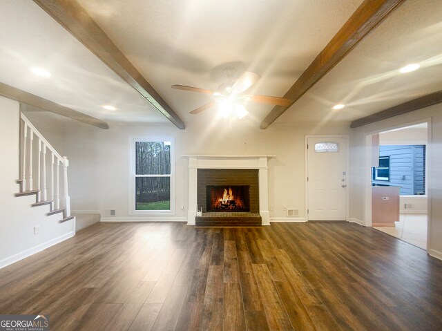 unfurnished living room featuring beam ceiling, ceiling fan, a brick fireplace, and dark wood-type flooring