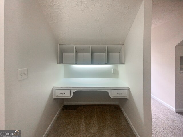 unfurnished office featuring a textured ceiling and dark colored carpet