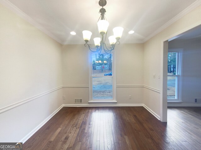 spare room with an inviting chandelier, ornamental molding, plenty of natural light, and dark wood-type flooring