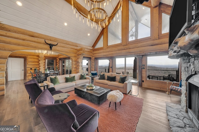 living room featuring high vaulted ceiling, a stone fireplace, a notable chandelier, log walls, and light wood-type flooring