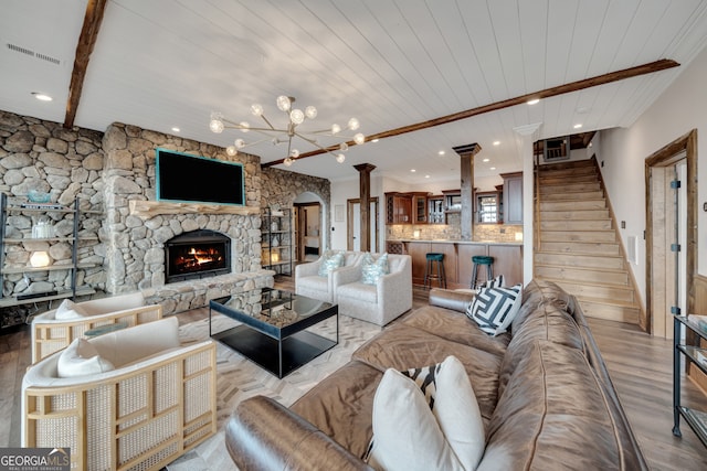 living room featuring decorative columns, light hardwood / wood-style flooring, an inviting chandelier, beam ceiling, and a stone fireplace