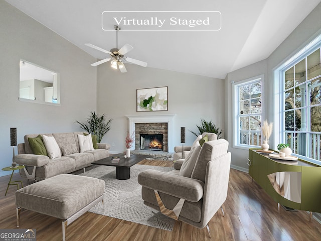 living room featuring dark hardwood / wood-style flooring, ceiling fan, a stone fireplace, and vaulted ceiling