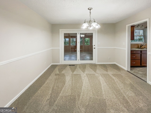 carpeted spare room featuring an inviting chandelier, sink, a textured ceiling, and a healthy amount of sunlight