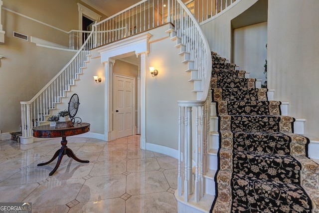 stairs with light tile flooring, ornamental molding, a towering ceiling, and ornate columns