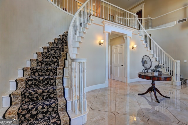 staircase with crown molding, a high ceiling, light tile floors, and ornate columns