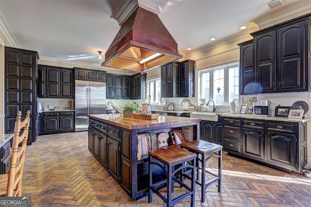 kitchen with crown molding, built in refrigerator, a kitchen island, and custom exhaust hood