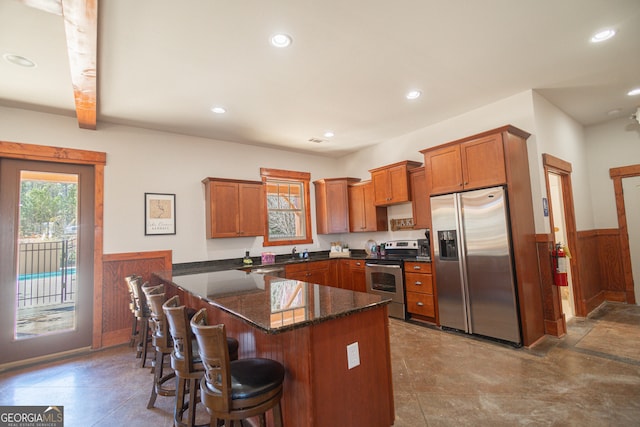 kitchen with a kitchen breakfast bar, tile flooring, kitchen peninsula, stainless steel appliances, and dark stone countertops