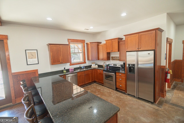 kitchen featuring dark stone counters, kitchen peninsula, a breakfast bar area, dark tile floors, and appliances with stainless steel finishes