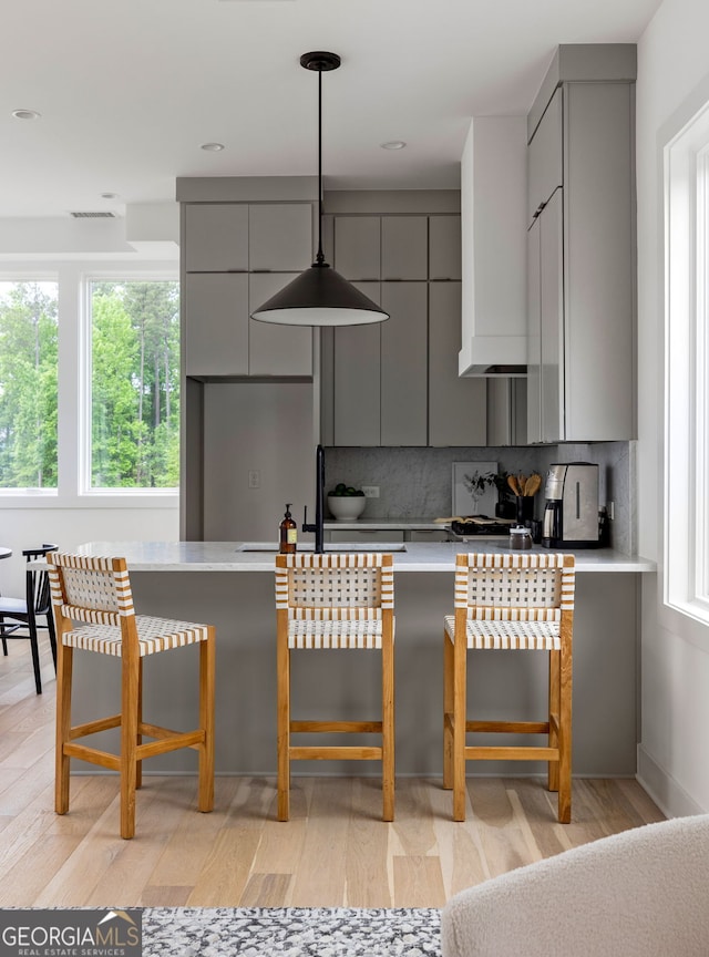 kitchen featuring gray cabinets, light wood-type flooring, decorative backsplash, and a kitchen breakfast bar