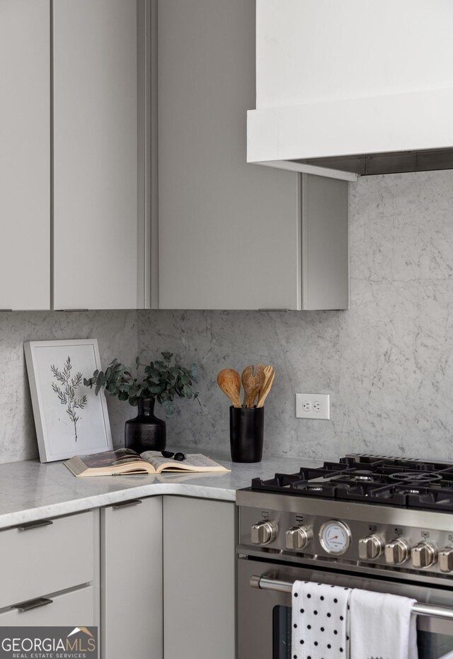 kitchen featuring high end stainless steel range oven, decorative backsplash, exhaust hood, and gray cabinets