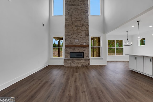 unfurnished living room featuring a fireplace, a high ceiling, a chandelier, and dark wood-type flooring